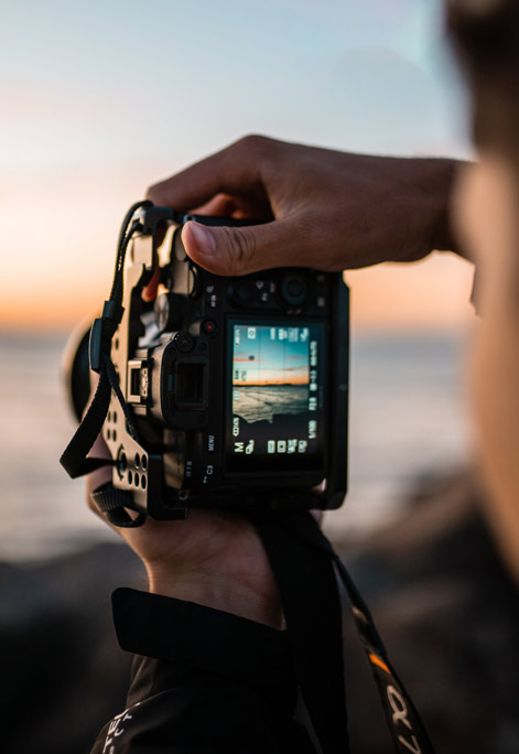 Person steht am Strand und fotografiert. Blick über die Schulter auf das Dispay der Kamera.